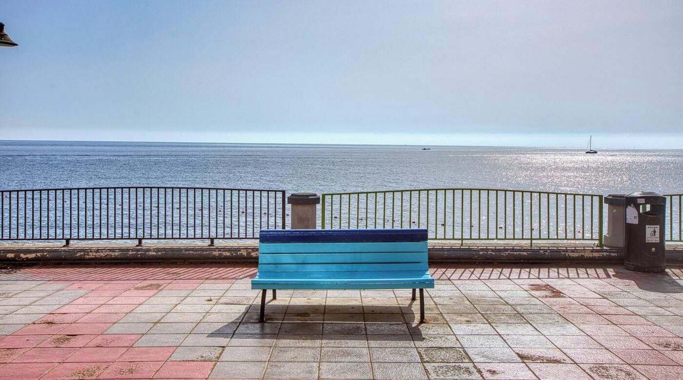 A bench facing a waterfront with a railing and a trash bin.