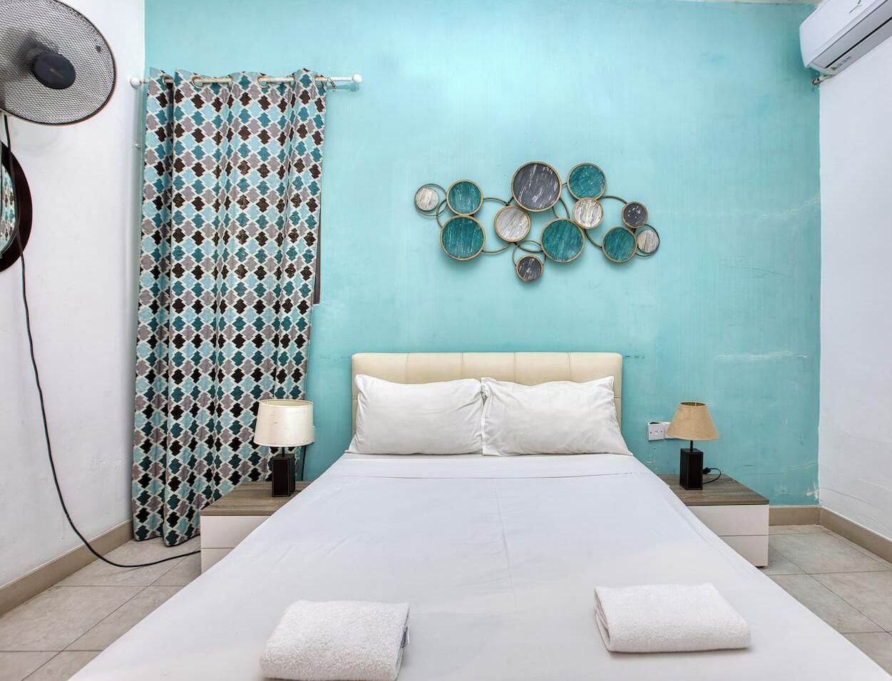Una camera da letto con un letto, due comodini, una ventola a parete, una tenda e un elemento decorativo a parete.
