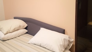 A bed with striped bedding and two pillows, a dark headboard, and a plain wall. - Small Apartments City Center Retreat (Sarajevo)