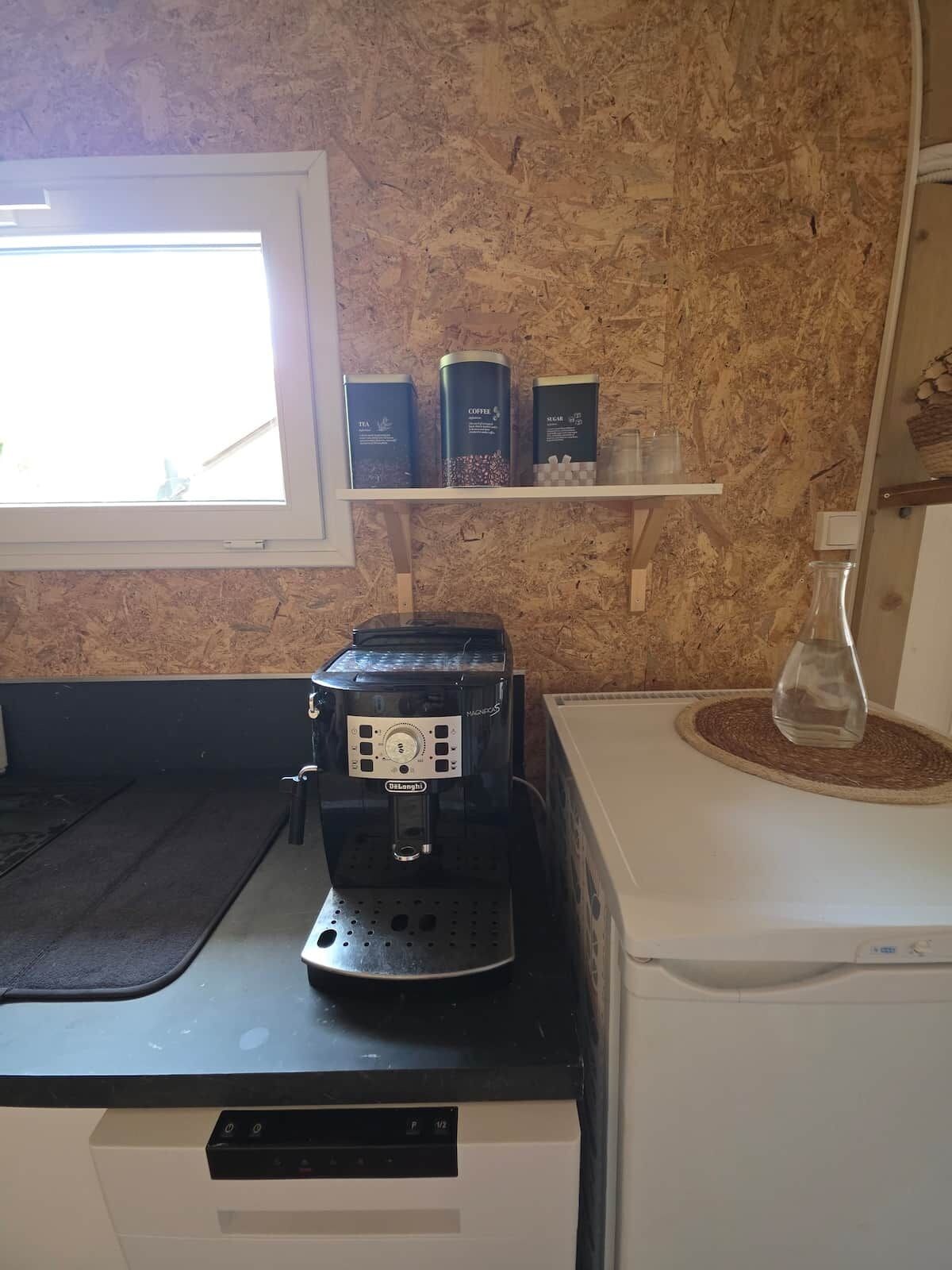 A kitchen area with a coffee maker, a shelf with containers, and a window.