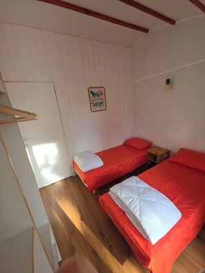 A room with two beds, wooden flooring, a white door, and a small table.