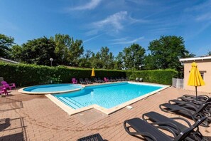 A rectangular swimming pool with a brick deck, surrounded by lounge chairs and umbrellas.
