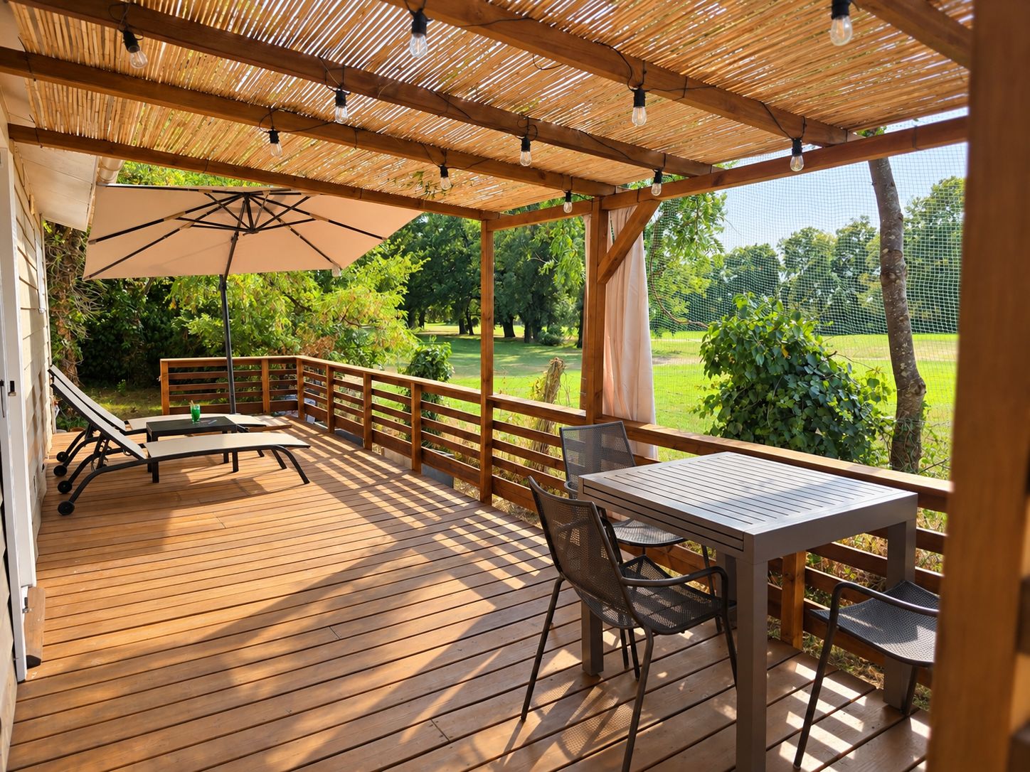 Une terrasse en bois avec une table et des chaises, un banc et une pergola décorée de guirlandes lumineuses.
