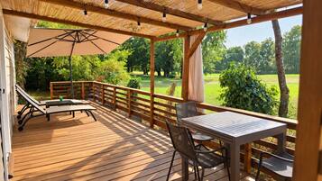 Une terrasse en bois avec une table et des chaises, un banc et une pergola décorée de guirlandes lumineuses.