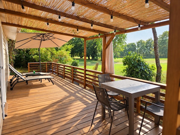 A wooden deck with a table and chairs, a bench, and a pergola with string lights.