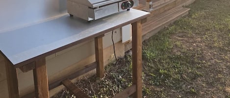 A portable grill on a wooden table outside a house.
