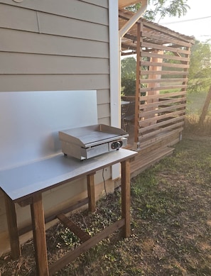 A portable grill on a wooden table outside a house.