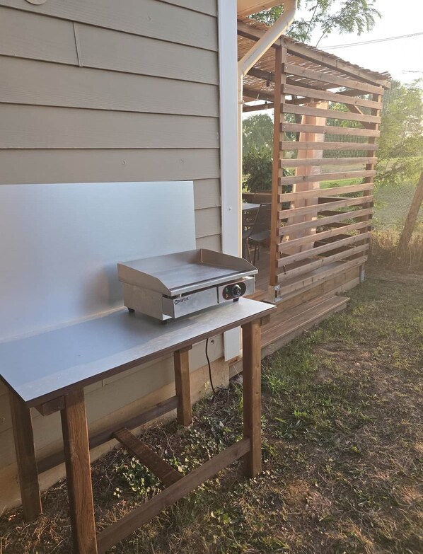 A portable grill on a wooden table outside a house.
