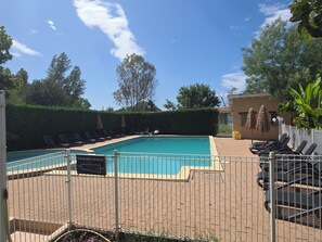 A swimming pool with lounge chairs and umbrellas, surrounded by a fence and greenery.