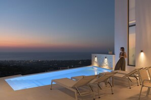 Ein moderner Poolbereich im Freien mit Liegestühlen und Blick auf die Stadt in der Dämmerung.