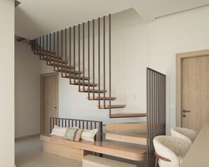 Een moderne trap met houten treden en metalen leuningen, die uitkomt op een plateau met een bank en een stoel.