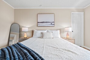 A bedroom with a bed, two bedside tables, a nightstand, a mirror, a door, and a framed picture on the wall. - Waterfront 5BR Estate w/ Heated Pool | Walk to Cocoa Beach (Cocoa Beach)
