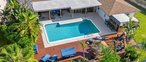 Un área de piscina en la azotea con una piscina rectangular, sillas de descanso y un espacio de estar cubierto.