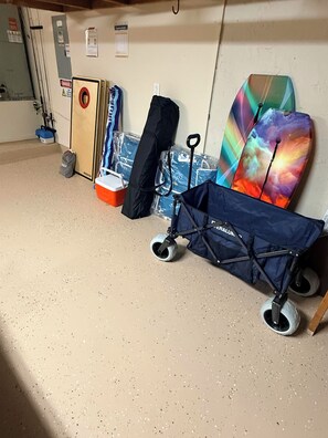 A storage area with various items including a blue umbrella, a colorful surfboard, and a wheeled cart. - Waterfront 5BR Estate w/ Heated Pool | Walk to Cocoa Beach (Cocoa Beach)
