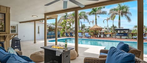 Ein Poolbereich mit Korbmöbeln, einem Deckenventilator und Blick auf Pool und Palmen.