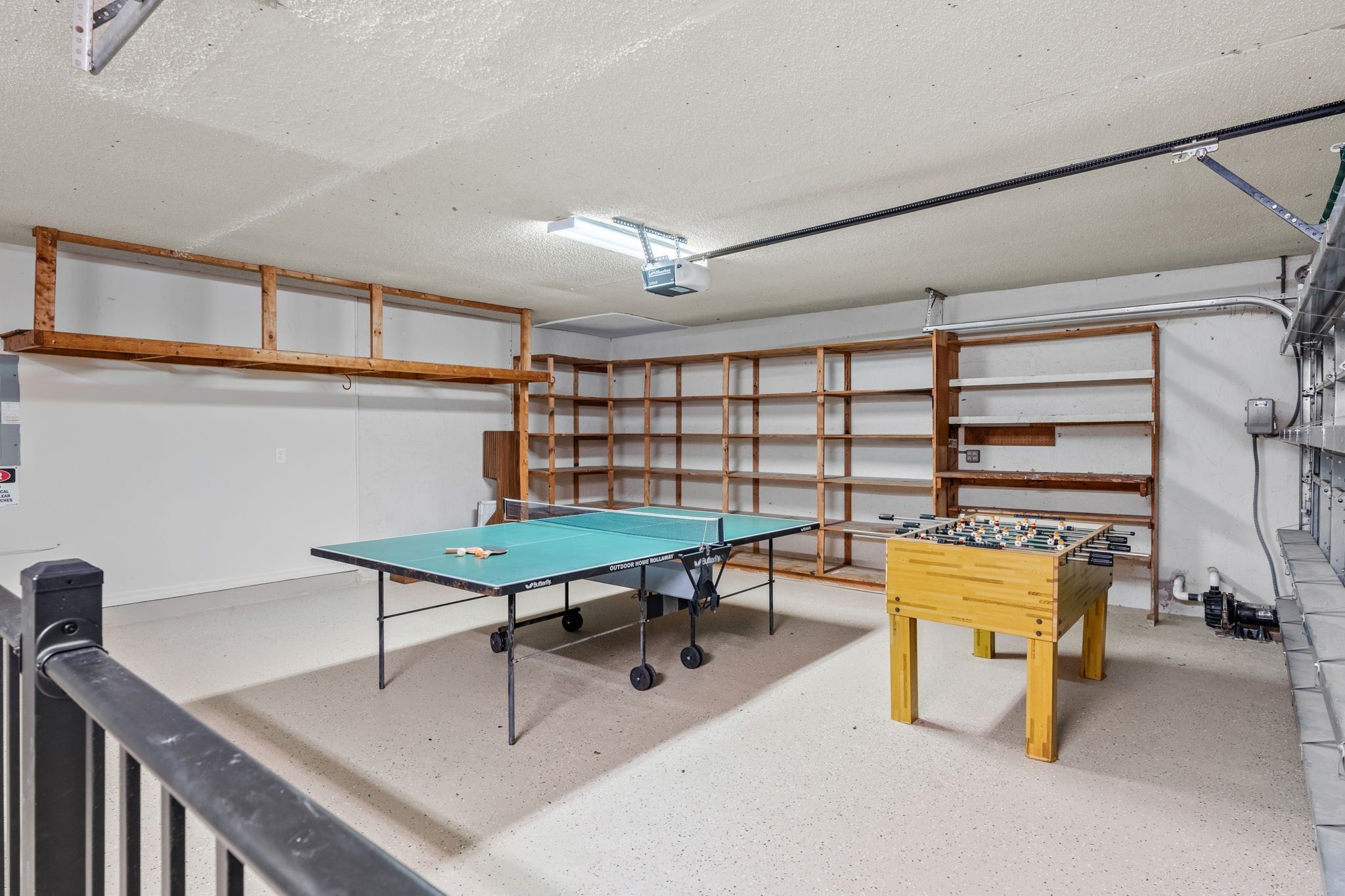 A room with a foosball table, a ping pong table, and a wooden shelf unit.