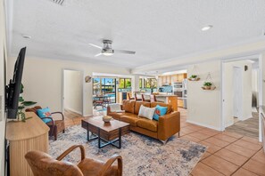 A spacious living room with a brown leather sofa, a wooden coffee table, and a television. - Waterfront 5BR Estate w/ Heated Pool | Walk to Cocoa Beach (Cocoa Beach)