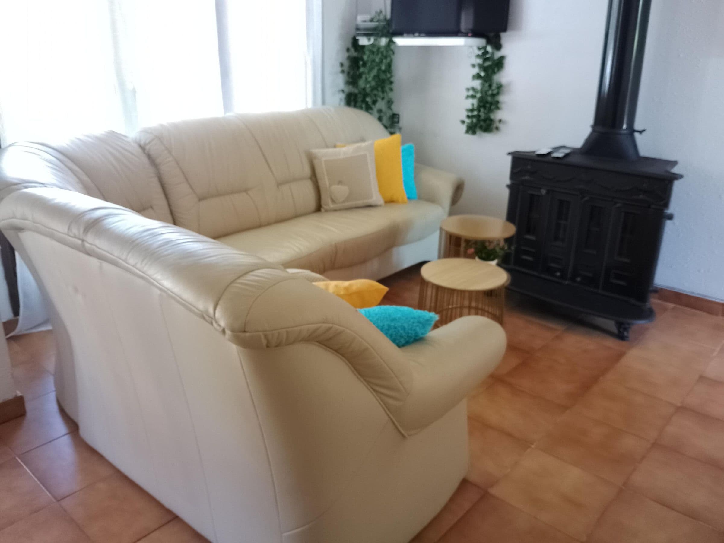 Um sofá bege com uma almofada, uma mesa redonda pequena e um armário preto com lareira.