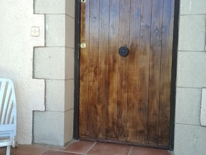 Eine Holztür mit Metallbeschlägen und Schlüsselloch, eingebettet in eine Ecke mit einem weißen Stuhl und einer Steinwand.