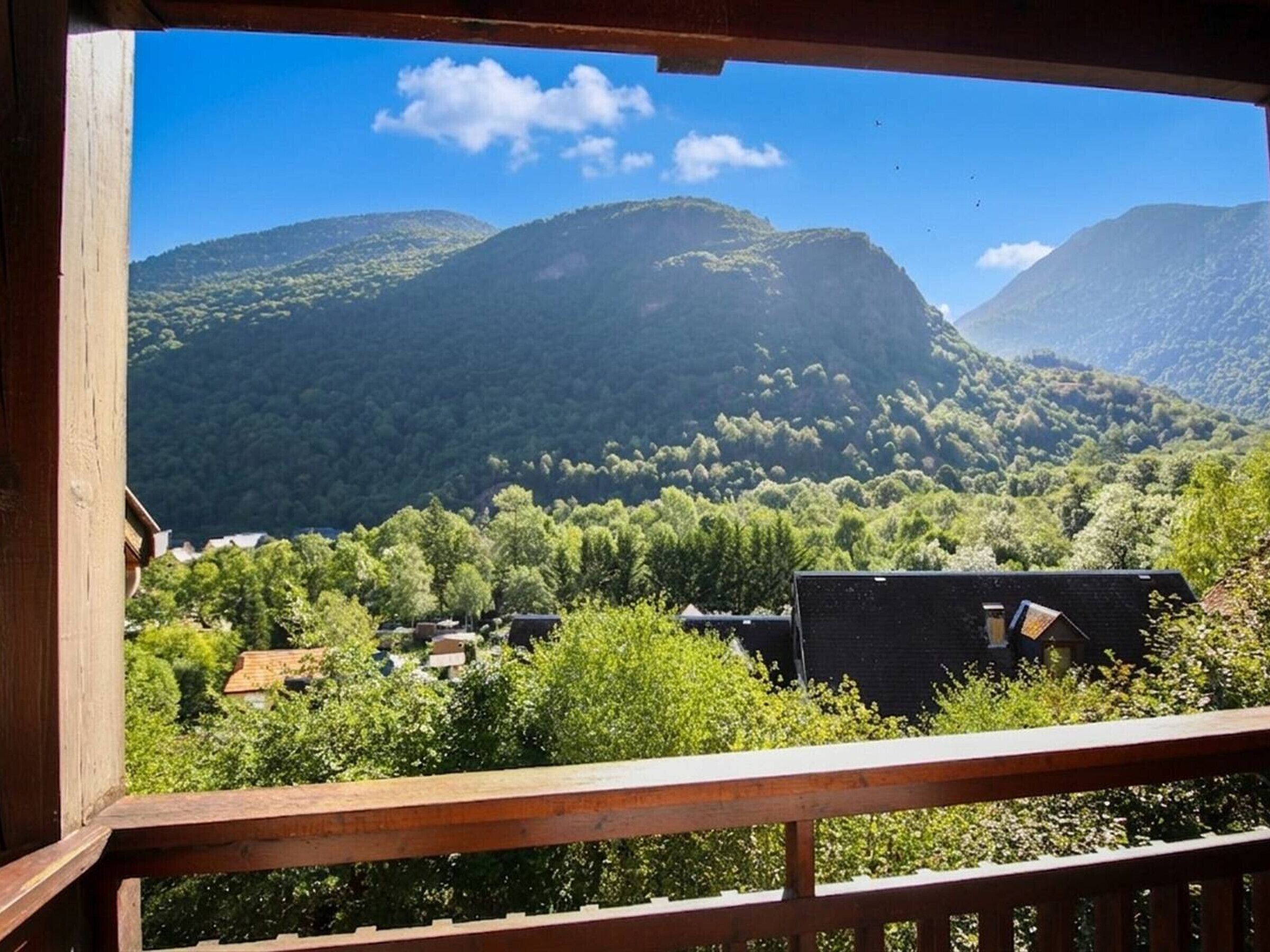 A view from a balcony overlooking a mountainous landscape with dense greenery and a clear sky.