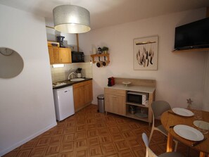 A compact kitchen with wooden cabinets, a microwave, a sink, and a dining area with a table set for two. - Quiet apartment with parking, pets OK - 4 guests, mountain view (Bagnères-de-Luchon)