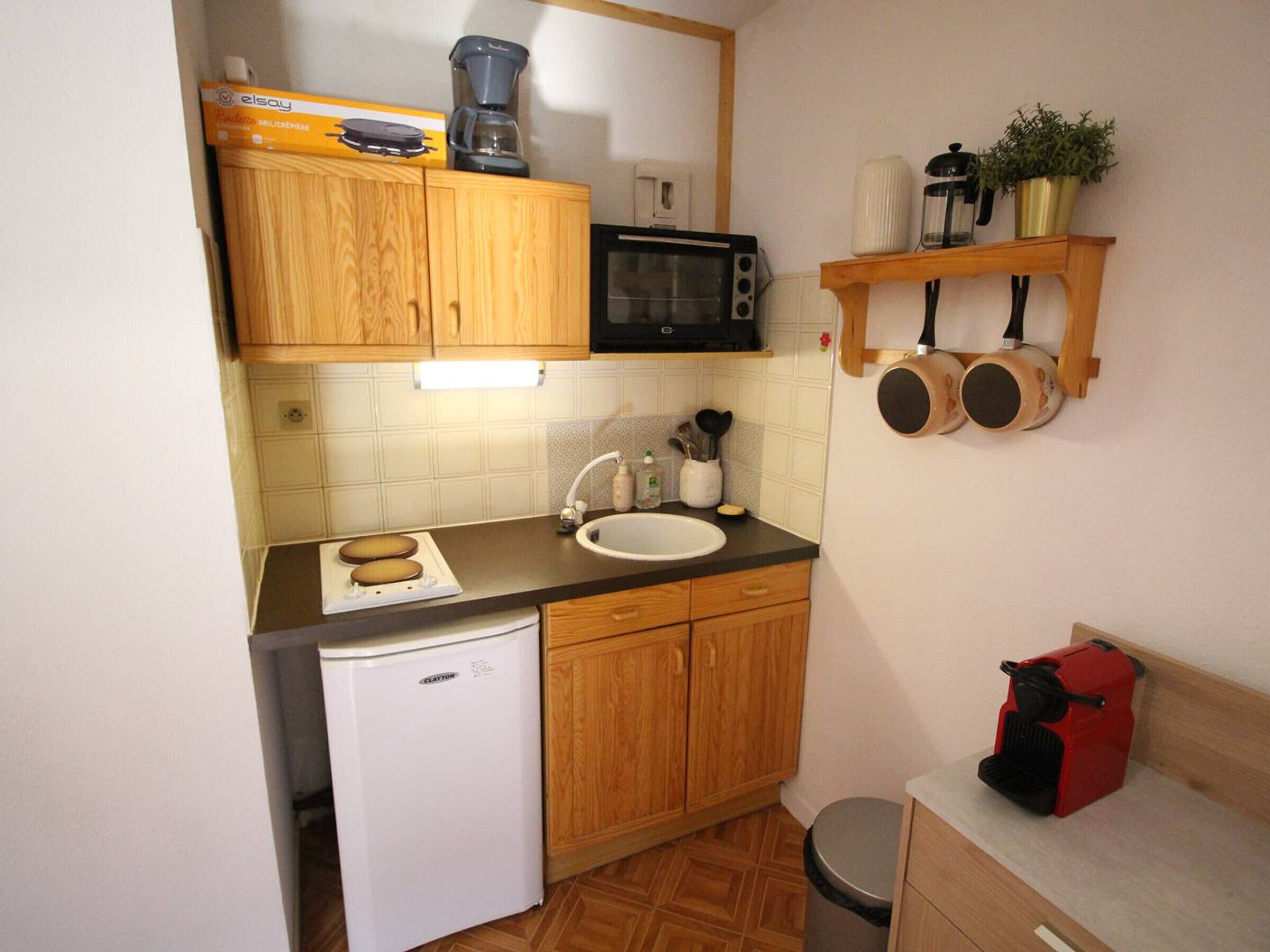 Eine kompakte Küche mit Holdekor-Schränken, einer Mikrowelle, einer Kaffeemaschine, einem Spülbecken und einem kleinen Kühlschrank.