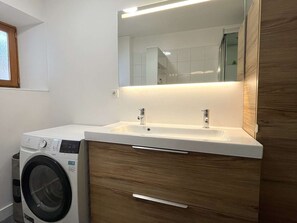 Ein kleines Badezimmer mit Waschmaschine, Waschbecken und Spiegel.