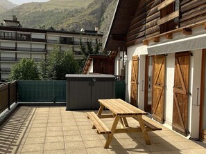 En træterrasse med et picnicbord og et udhus, med udsigt over et bjergrigt landskab.