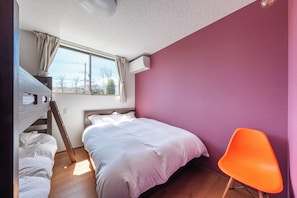 Ein Schlafzimmer mit Etagenbett, einem Einzelbett, einem Fenster mit Vorhängen, einer Klimaanlage und einem leuchtend orangefarbenen Sessel.