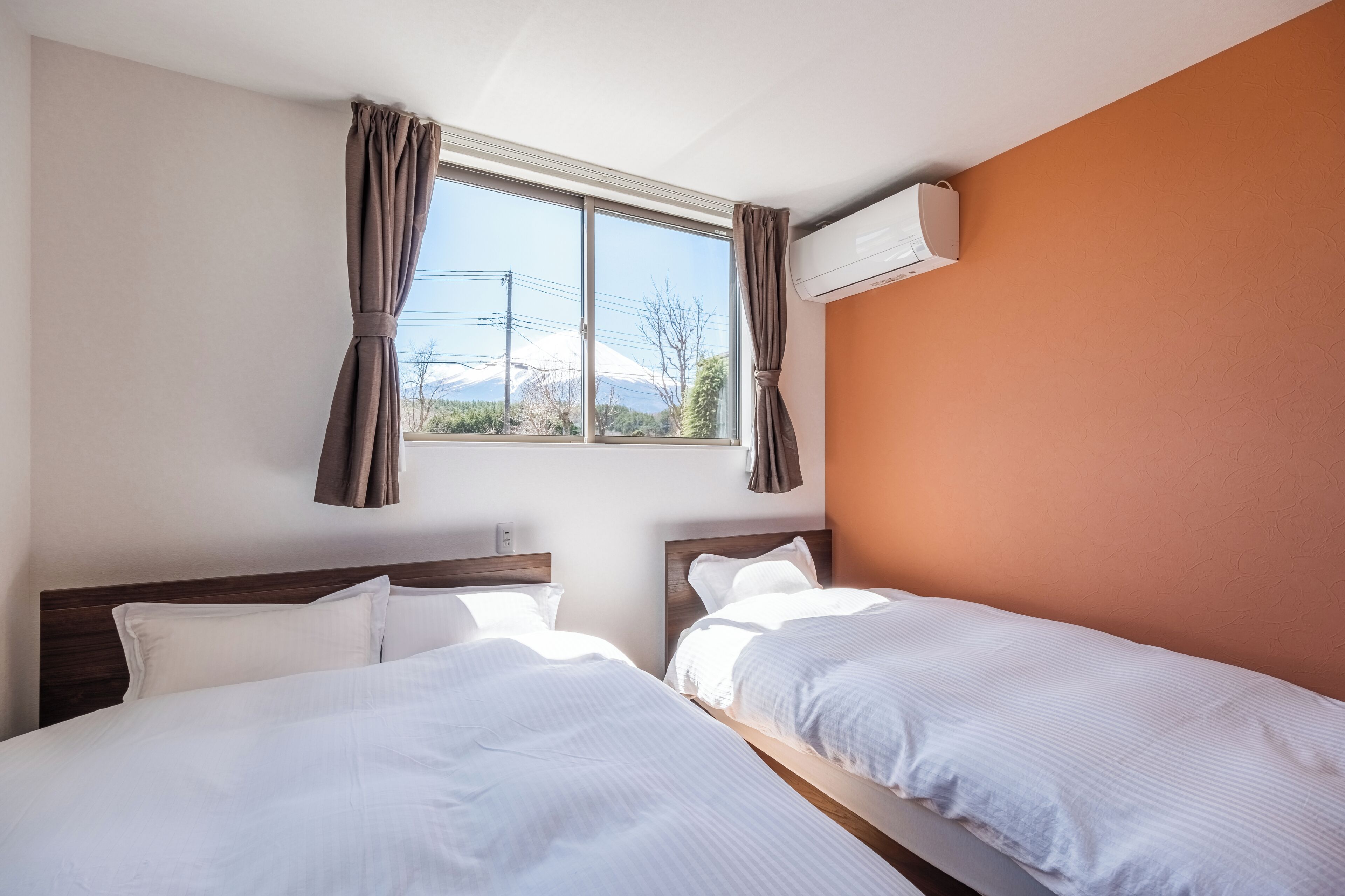 Une chambre d’hôtel avec deux lits, une fenêtre avec des rideaux, un appareil de climatisation et une vue sur une montagne.