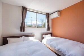 A hotel room with two beds, a window with curtains, an air conditioning unit, and a view of a mountain.