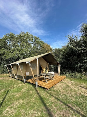Une tente dotée d’une terrasse en bois et d’une table, entourée d’arbres.
