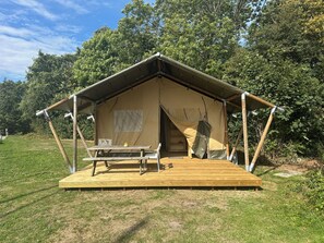 A tent with a picnic table and a small shelf, set in a grassy area with trees in the background.
