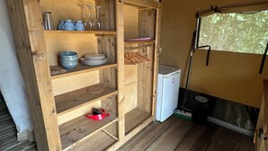 A compact kitchen area with wooden shelves, a small refrigerator, and a window with a view.
