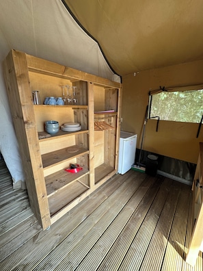 A compact kitchen area with wooden shelves, a small refrigerator, and a window with a view.
