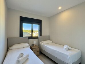 A hotel room with two single beds, a nightstand with a lamp, and a window with a view of the beach. - Apartment with panoramic view - 6 guests (Benidorm)