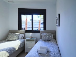 Ein Schlafzimmer mit zwei Betten, einem Fenster, einem Nachttisch und einem an der Wand hängenden Bild.
