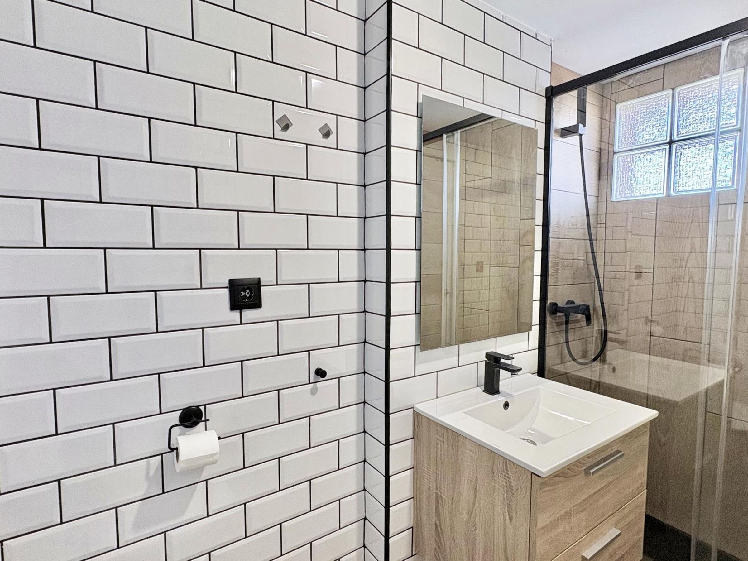 A bathroom with white tiled walls, a mirror, a sink, and a shower enclosure.