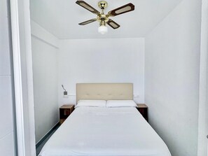 Ein schmales Hotelzimmer mit einem Einzelbett, einem Deckenventilator und einem Nachttisch.