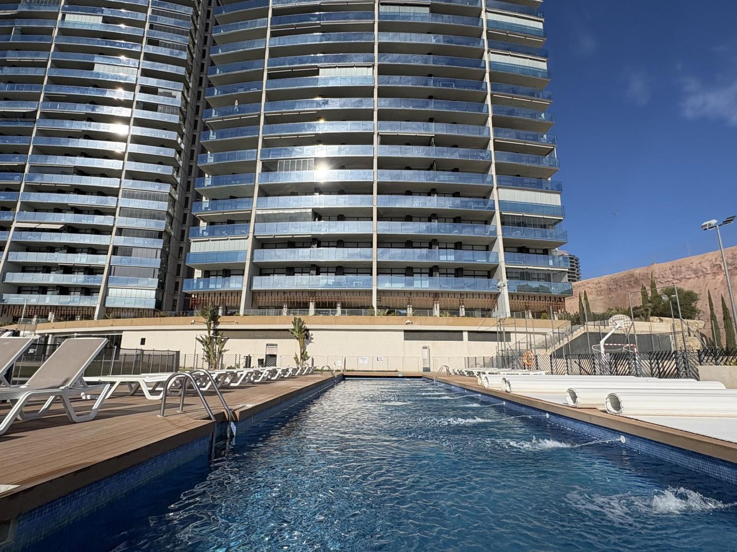 Ein modernes Hotel mit Poolbereich, das ein großes Freibad mit Holzterrasse und Liegestühlen zeigt.
