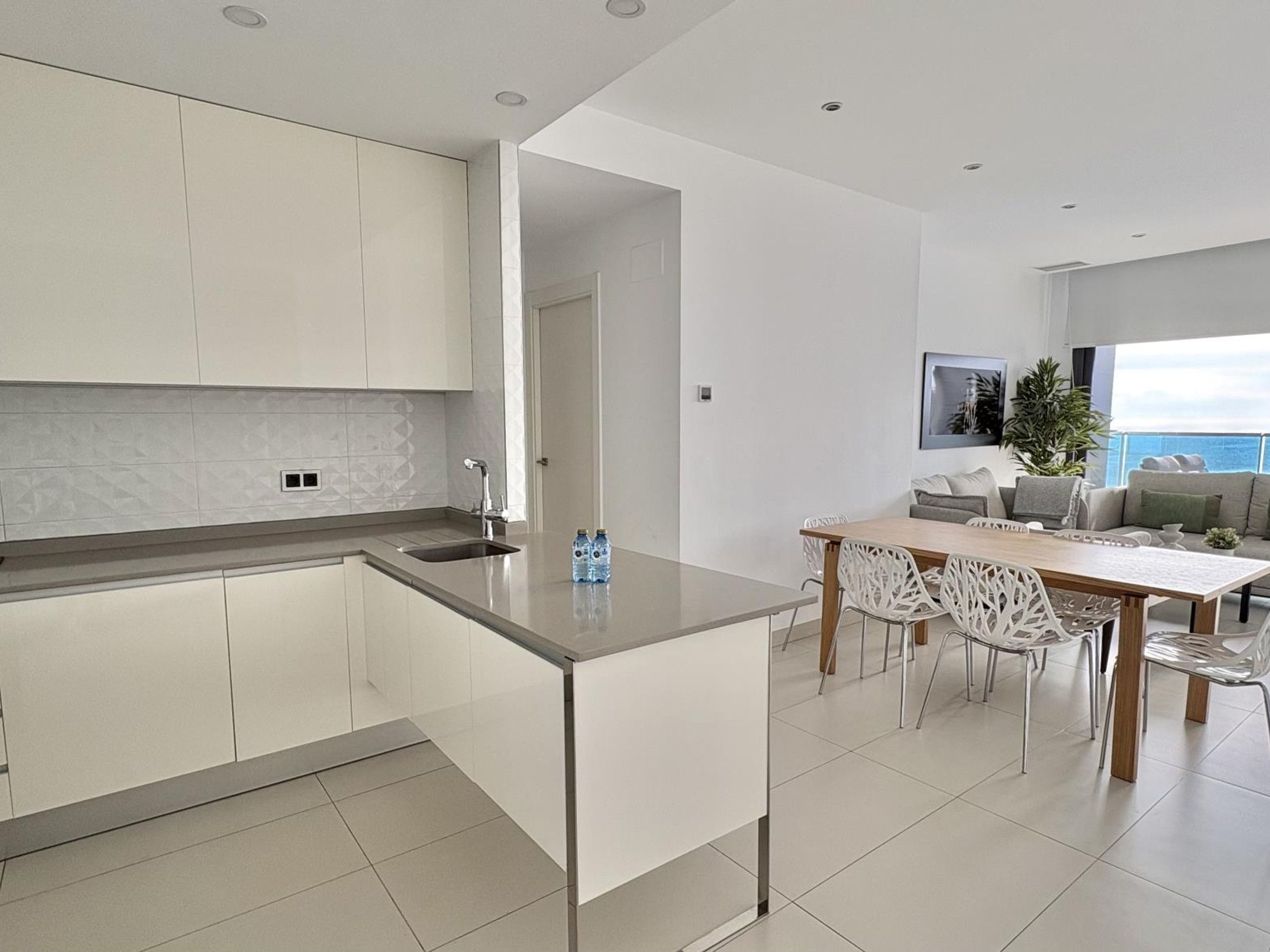 Une cuisine moderne avec des meubles blancs, un îlot central et un coin repas comprenant une table et des chaises.