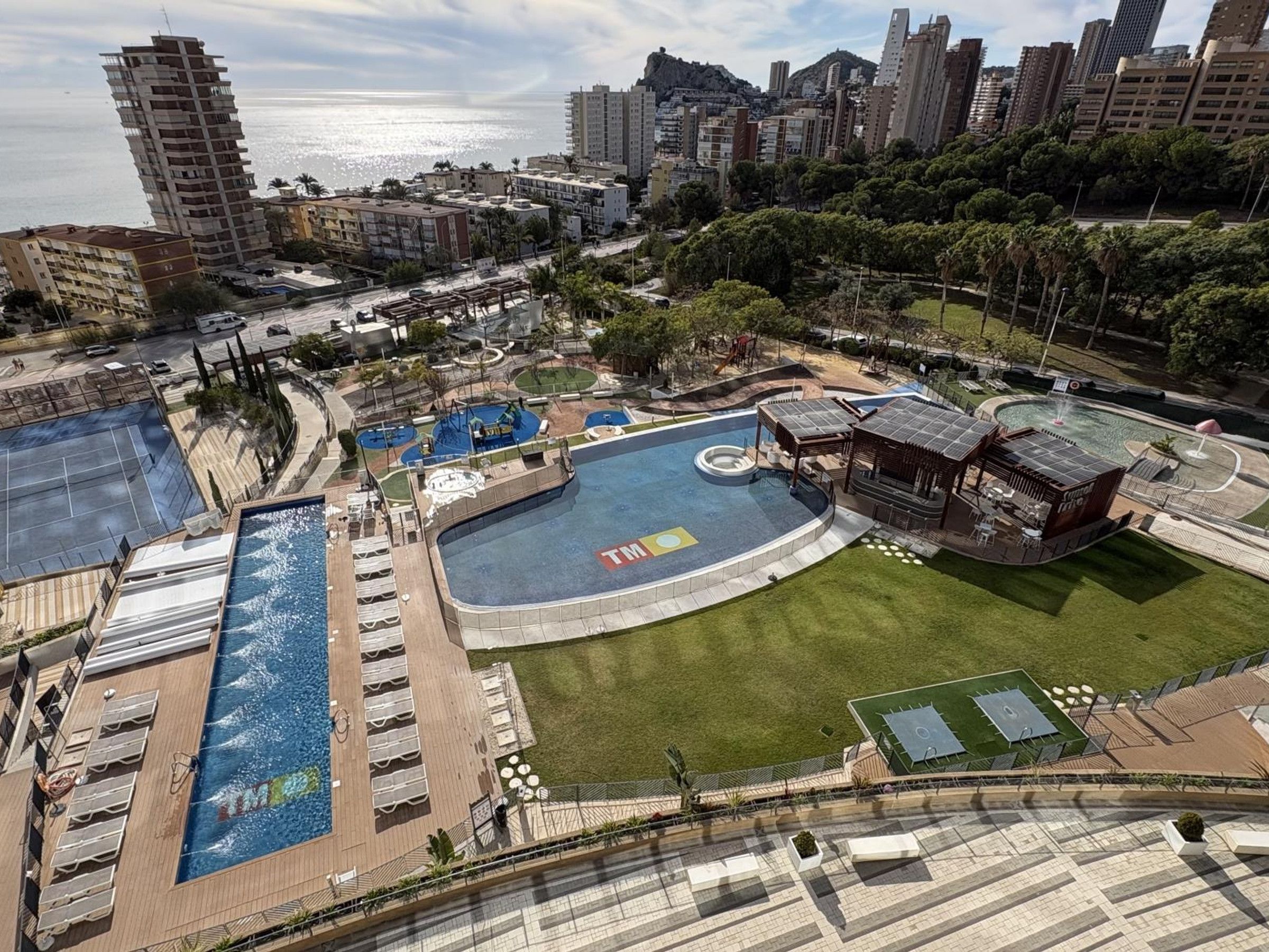 A residential area with a large swimming pool, tennis courts, and a gazebo.