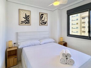 Habitació d'hotel amb un llit, dues obres d'art penjades a la paret, una finestra amb vista a edificis i un ventilador de sostre.