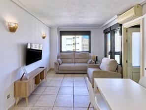 A living room with a flat-screen TV, two sofas, a wooden console table, and a dining table. - Modern apartment near the beach - 4 guests (Villajoyosa)