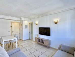 A modern living room with a flat-screen TV mounted on the wall, a dining area with a white table and chairs, and a sofa. - Modern apartment near the beach - 4 guests (Villajoyosa)
