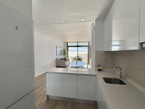Eine moderne Küche mit einer zentralen Kochinsel, einem Essbereich mit rundem Tisch und Blick ins Freie durch große Fenster.