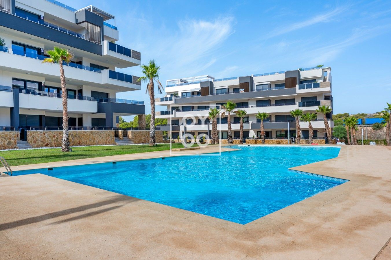 Ein modernes Hotel mit Schwimmbad, mehreren Balkonen und Palmen.