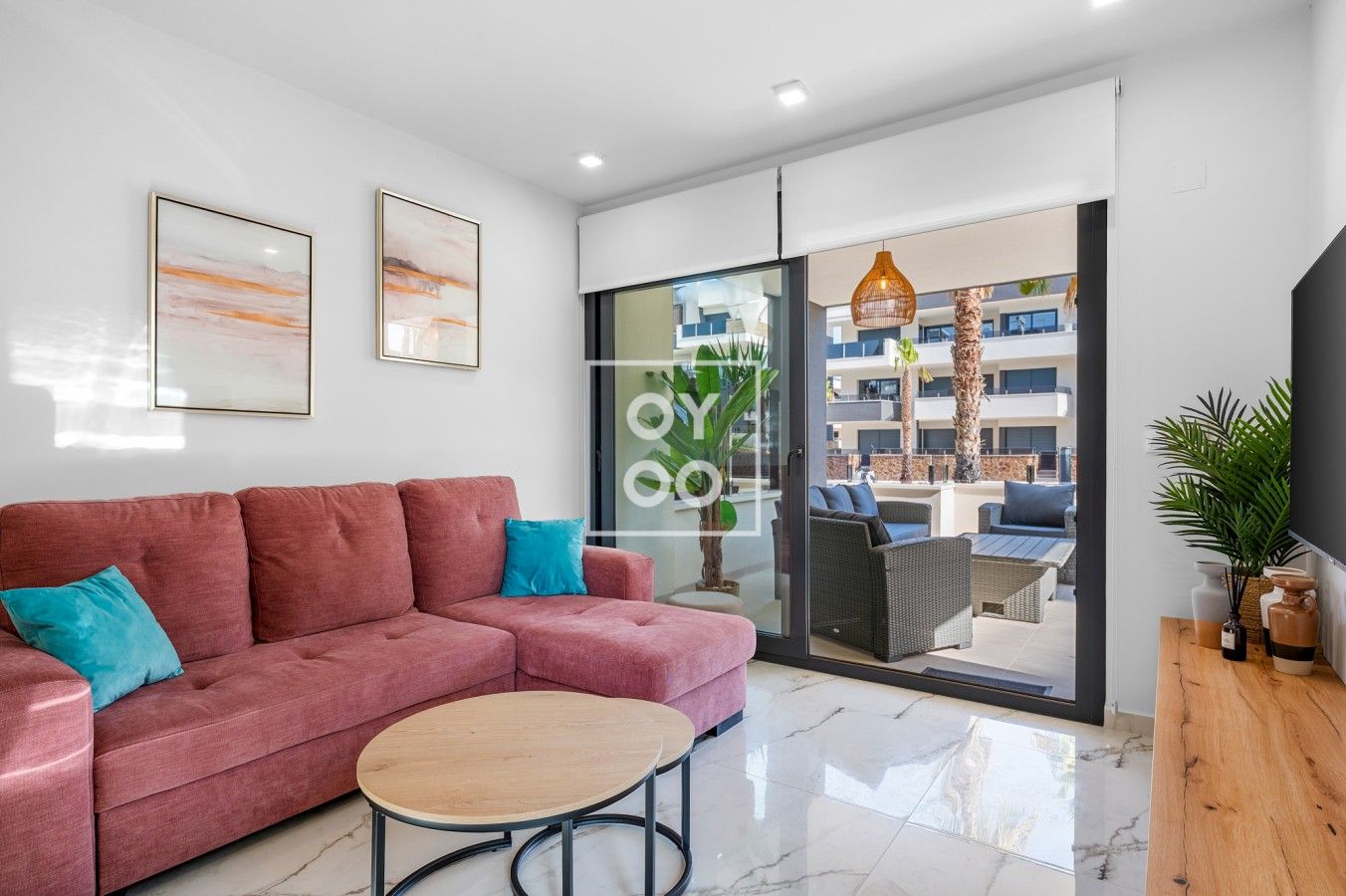 A modern living room with a pink sofa, a round coffee table, and a glass door leading to an outdoor seating area.