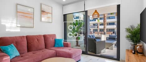A modern living room with a pink sofa, a round coffee table, and a glass door leading to an outdoor seating area.