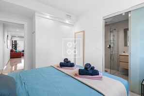 Ein modernes Hotelzimmer mit einem großen Bett, einer Duschkabine und Blick in den Wohnbereich.